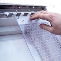 Perforated PVC strip door Hand hanging perforated PVC strips onto a mounting rail