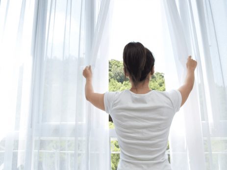 Woman opening curtains at a bright window to let in fresh air