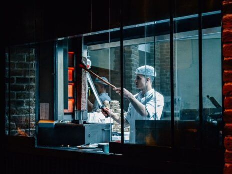 Chef working in a commercial kitchen seen through a window at night